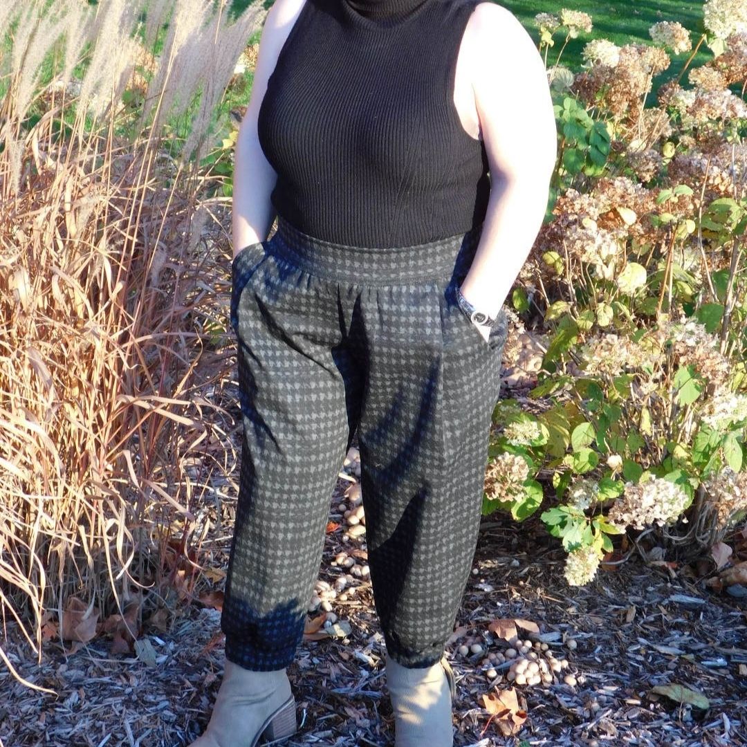 Model with dwarfism wearing dark ankle-length pants outdoors in a garden setting, side view